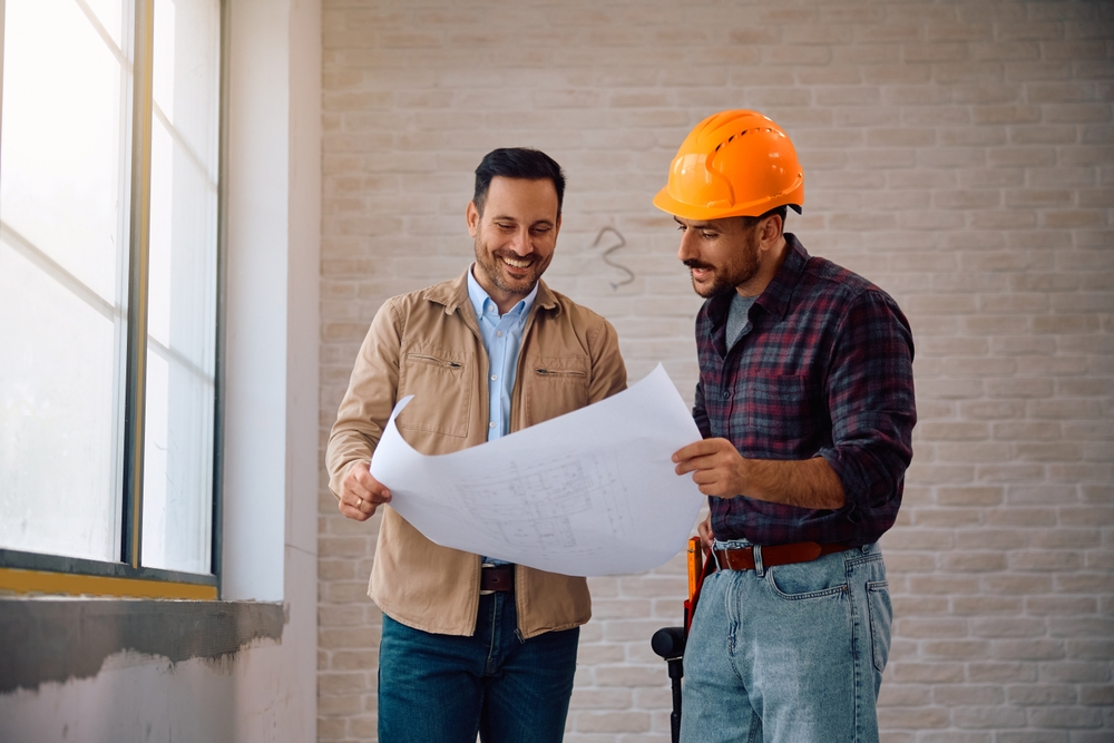 Happy,Home,Owner,And,Construction,Worker,Examining,Blueprints,During,Renovating